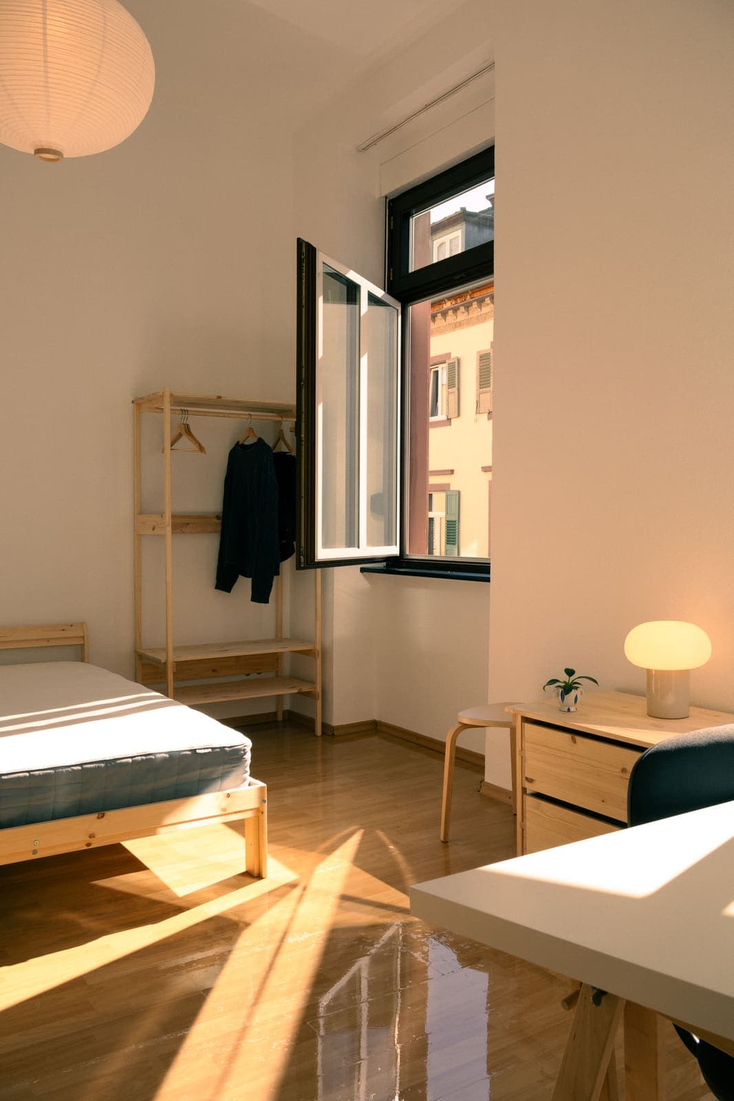 WG-Zimmer nach der Möblierung mit Bett und Kleiderstange am geöffneten Fenster